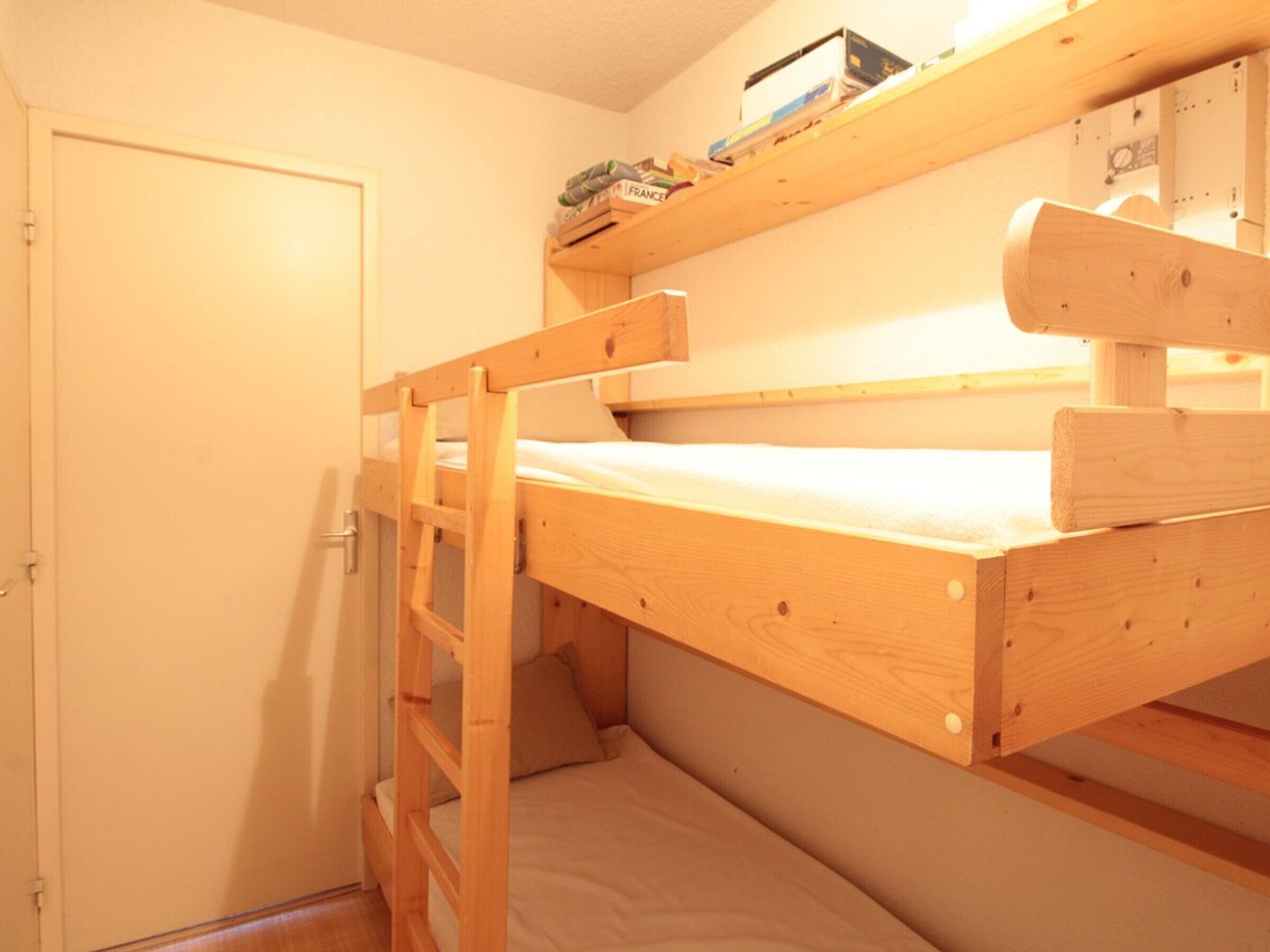 A bunk bed room with a door, a shelf above the bed, and a small window.