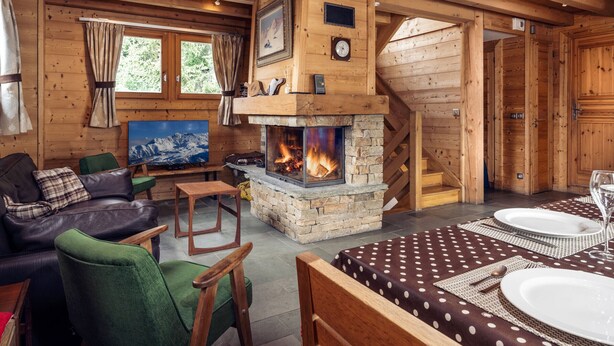 Een gezellig cabin interieur met een stenen openhaard, houten wanden, een eethoek met een tafelkleed met stippen, en een televisie op een houten standaard.