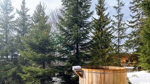 Een houten jacuzzi omringd door sneeuw en bomen.