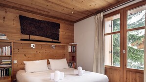 Een slaapkamer met houten lambrisering, een groot bed, boekenkasten en een raam met gordijnen.