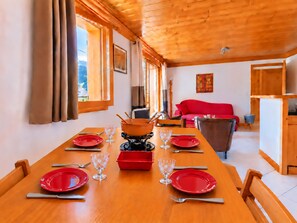 A dining area with a wooden table set for four, a red sofa in the background, and a wooden ceiling.