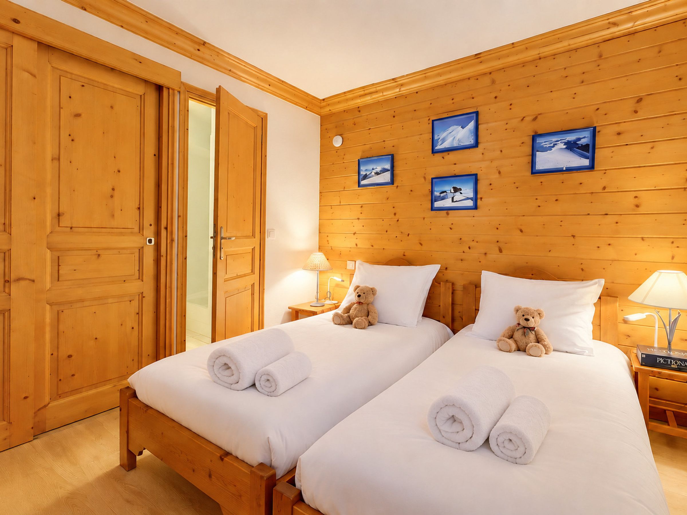 A hotel room with two beds, wooden walls, and framed pictures on the wall.