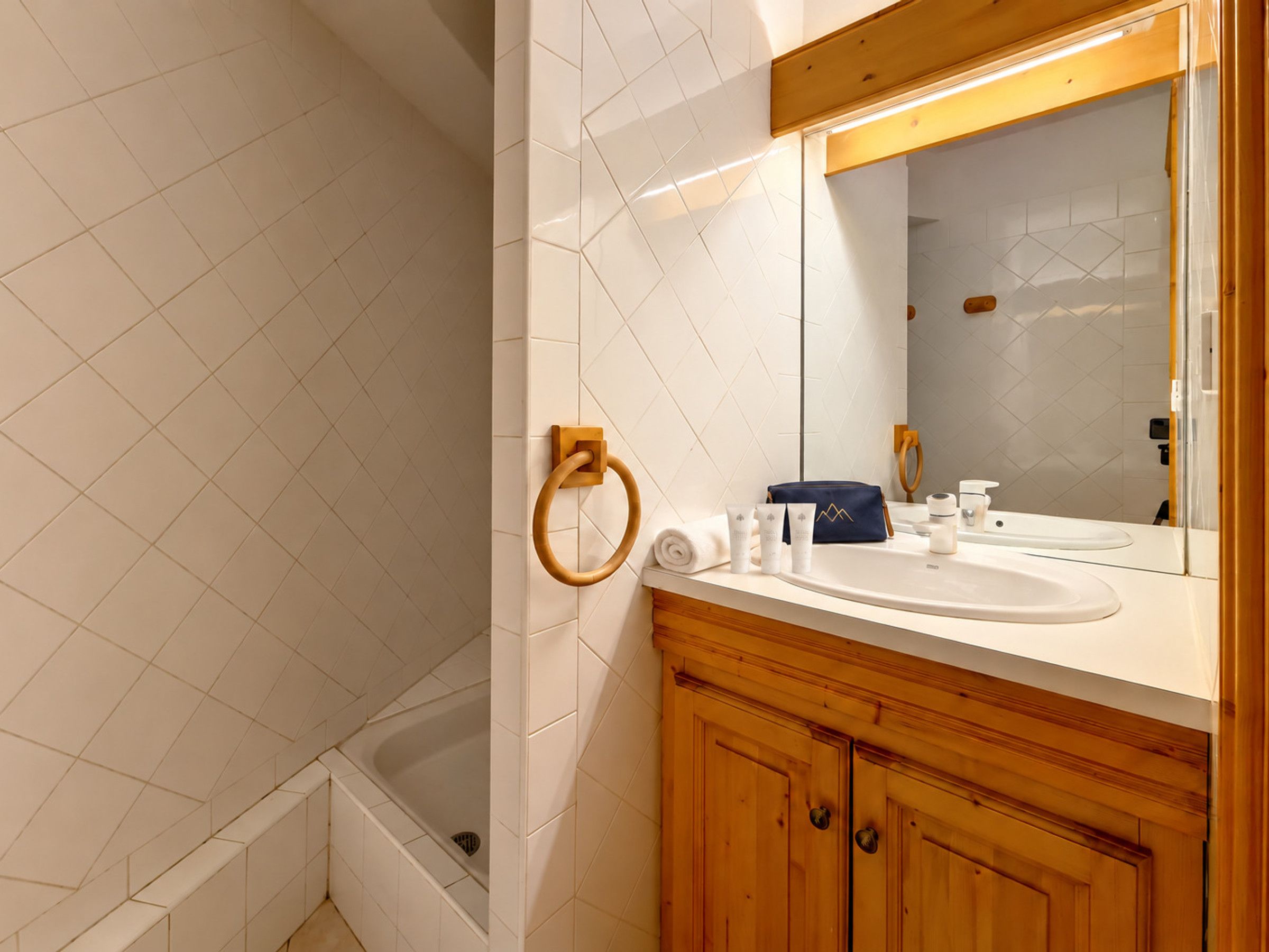 A modern bathroom with a wooden vanity, a large mirror, and a bathtub.