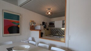 Una cocina moderna con armarios blancos, microondas y cafetera. Hay un comedor con una mesa y sillas blancas, y un tazón sobre la mesa.