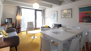 Una sala de estar moderna con un sofá, una mesa de comedor y sillas. Hay un televisor y una estantería.