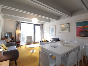 Una sala de estar moderna con un sofá, una mesa de comedor y sillas. Hay un televisor y una estantería.