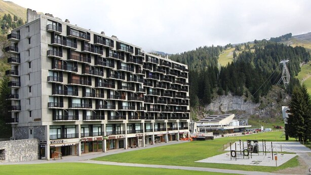 Un hotel de varios pisos con diseño moderno, que cuenta con balcones en cada planta, un patio central y vistas del paisaje montañoso circundante.