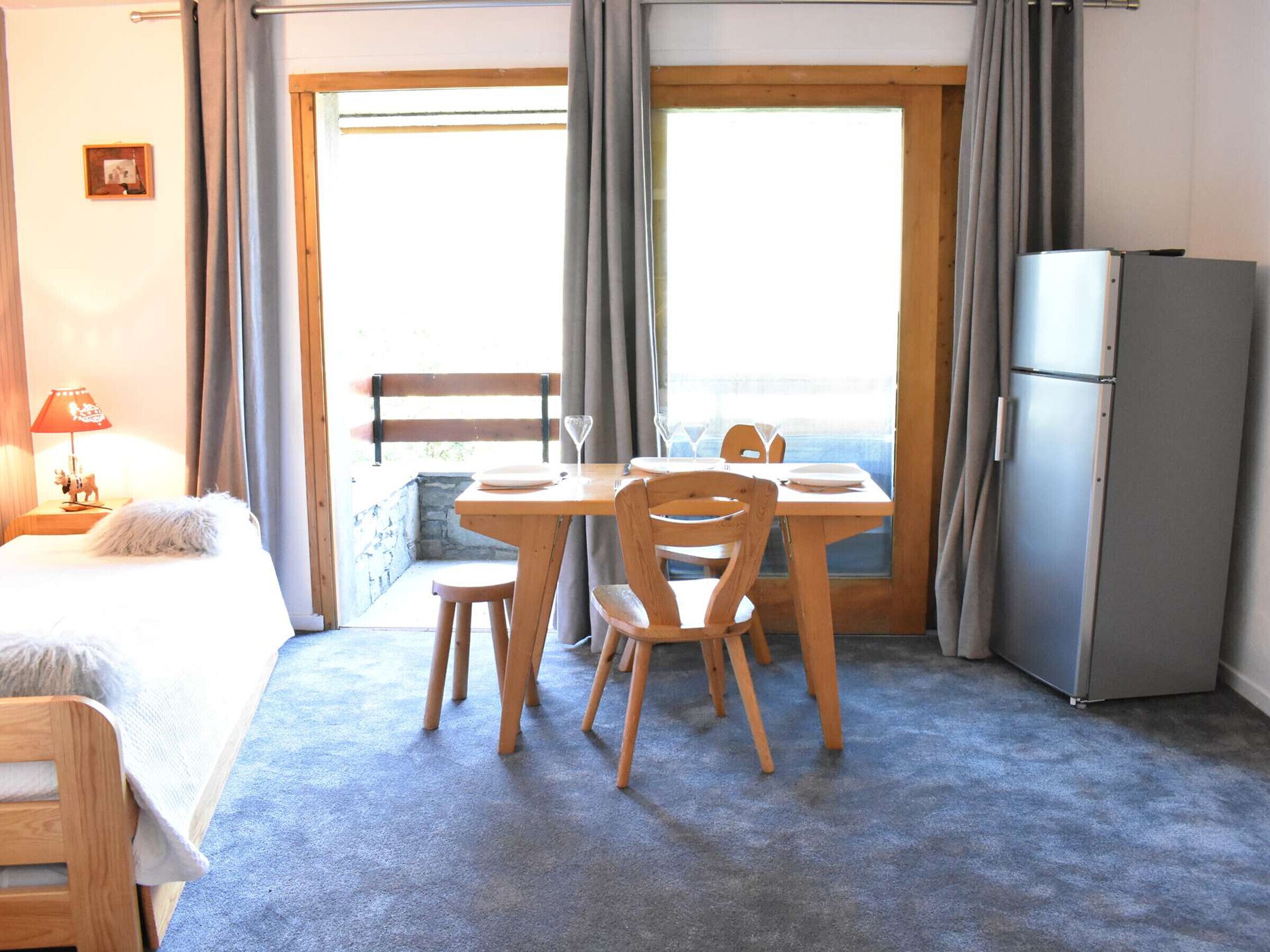 Ein Zimmer mit einem Bett, einem Tisch mit Stühlen, einem Kühlschrank und Blick durch ein Fenster.