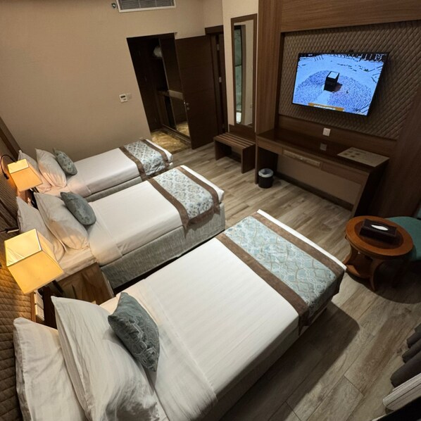 A hotel room with two beds, a TV on the wall, a small table, and a bench. - Midan Hotel (Makkah)