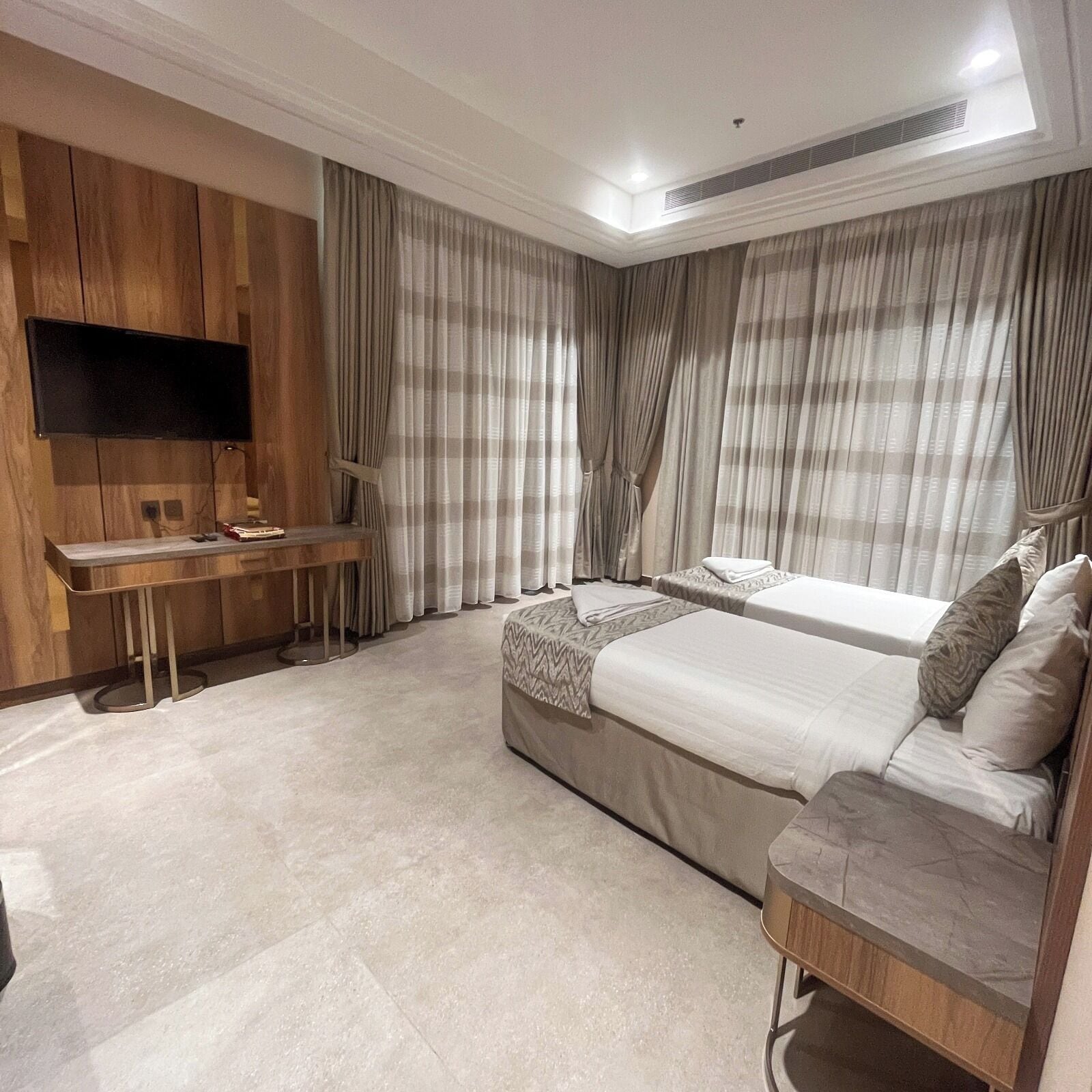 A modern bedroom with a flat-screen TV mounted on the wall, a desk, two beds, and a sofa.