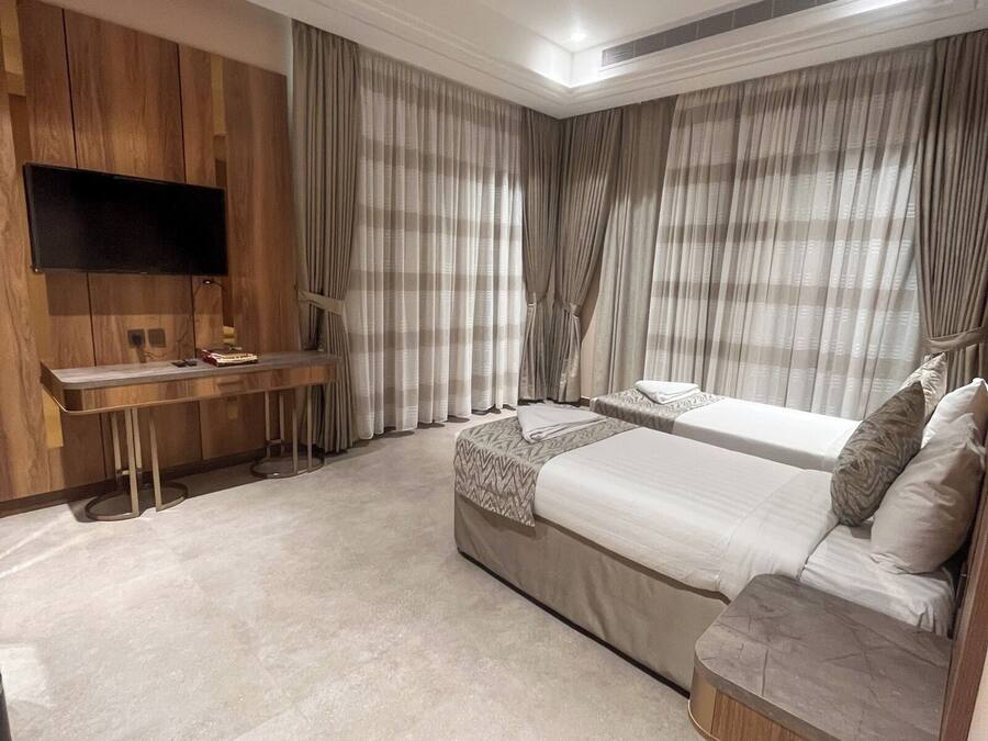 A modern bedroom with a flat-screen TV mounted on the wall, a desk, two beds, and a sofa.