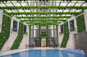 An indoor swimming pool with a glass ceiling, surrounded by walls covered in greenery, and furnished with outdoor-style chairs. - Midan Hotel (Makkah)