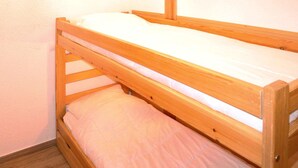 A single wooden bunk bed with a white mattress and a pink blanket.