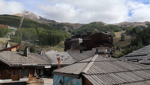 A rustic mountain village with traditional wooden buildings, a ski lift, and a view of the surrounding hills.