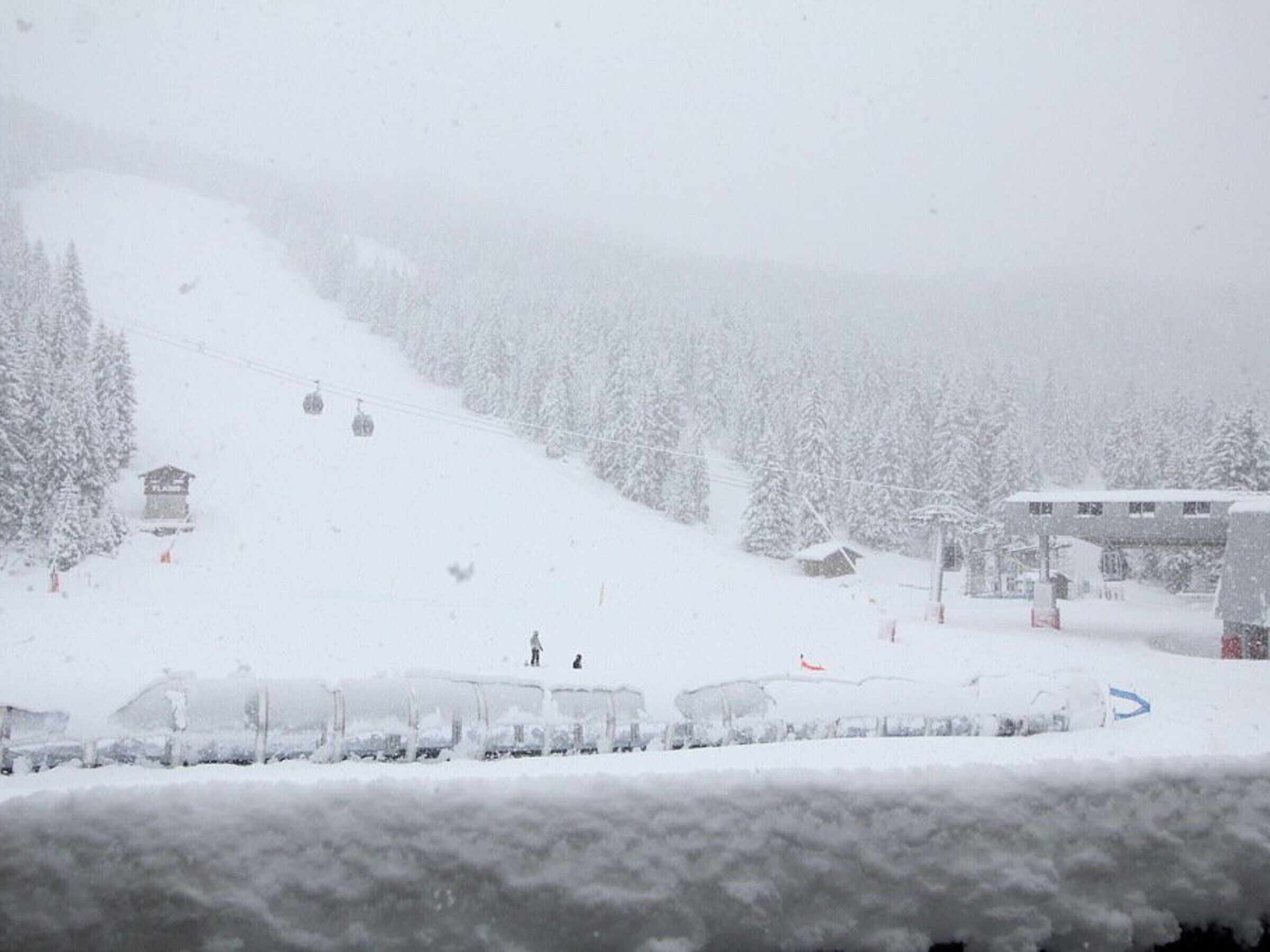 Une piste de ski enneigée, avec un télésiège, des bâtiments et des arbres.