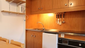 Eine kleine Küche mit Holzausstattung, einem weißen Kühlschrank, einer Spülmaschine und einem Herd.