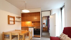 Ein kompakter Wohnbereich mit Küchenzeile, einem Essbereich mit Holztisch und Stühlen sowie einem roten Sofa.