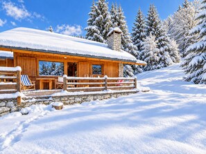 A wooden cabin with a stone foundation, a covered porch, and a view of snow-covered trees. - Méribel Chalet: Ski-in/Ski-out, spacious, bright with fireplace (Méribel)