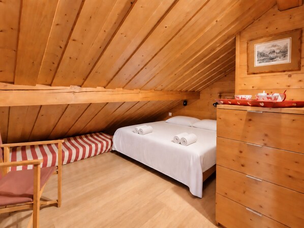 A cozy wooden room with a single bed, a dresser, and a small table with a picture on the wall.