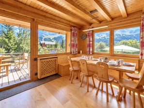A wooden cabin with a dining area, large windows, and a view of mountains.
