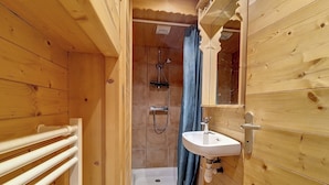 Un bany de fusta amb dutxa, un lavabo i un suport per a tovalloles.
