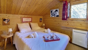 Un dormitori acollidor de cabana de fusta amb un llit, taules de nit i una finestra amb cortines.