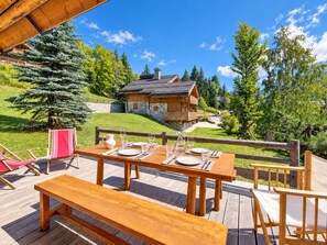 A wooden deck with a table set for dining, overlooking a mountainous landscape with a lodge.