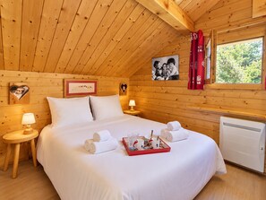 A wooden cabin bedroom with a bed, two bedside tables, a window, and a radiator.