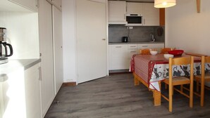 A compact kitchen with white cabinets, a microwave, and a coffee maker. There's a dining table with a red and white checkered tablecloth and wooden chairs. - Renovated Studio for 4, South-Facing Balcony, Close to Slopes & Shops (Flaine)