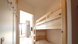 A room with bunk beds, a wooden floor, a door, and a window with curtains. - Renovated Studio for 4, South-Facing Balcony, Close to Slopes & Shops (Flaine)