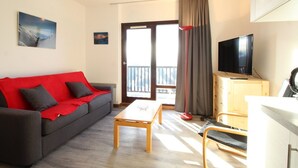 A living room with a sofa, a coffee table, a TV, and a balcony door. - Renovated Studio for 4, South-Facing Balcony, Close to Slopes & Shops (Flaine)