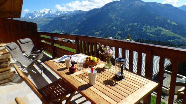 A wooden deck with a table set for two, overlooking a mountainous landscape.