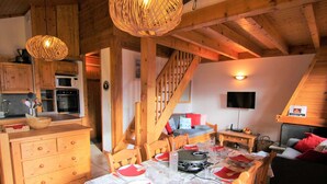 A cozy cabin-style room with a dining area, wooden furniture, a staircase, and a kitchen with wooden cabinets and appliances.