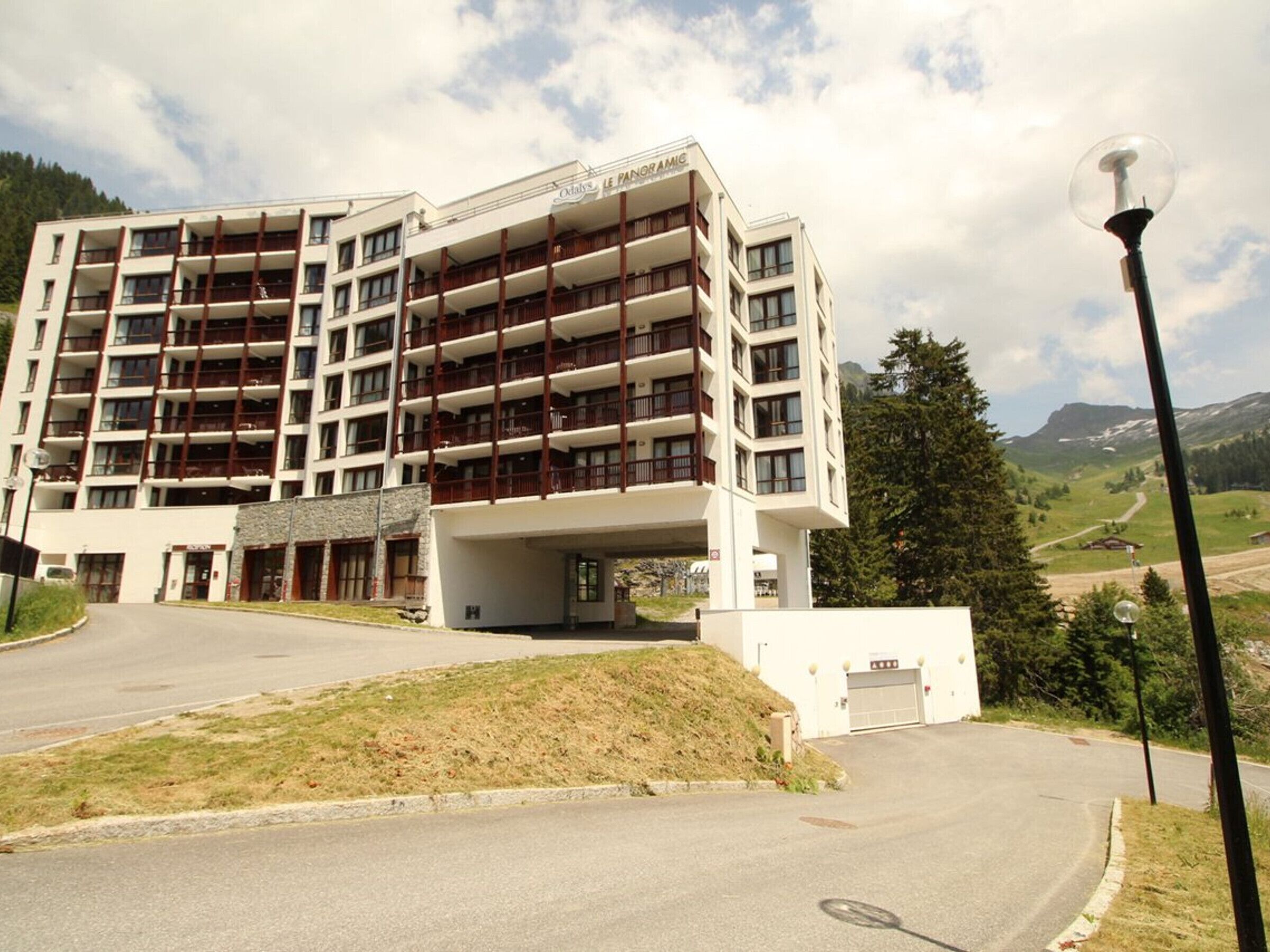 A multi-story hotel with balconies, a parking area, and a view of the surrounding landscape.