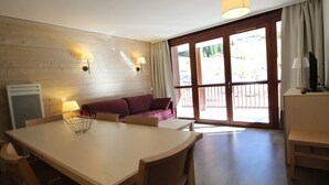 Een kamer met een houten tafel en stoelen, een bank en een groot raam met gordijnen.