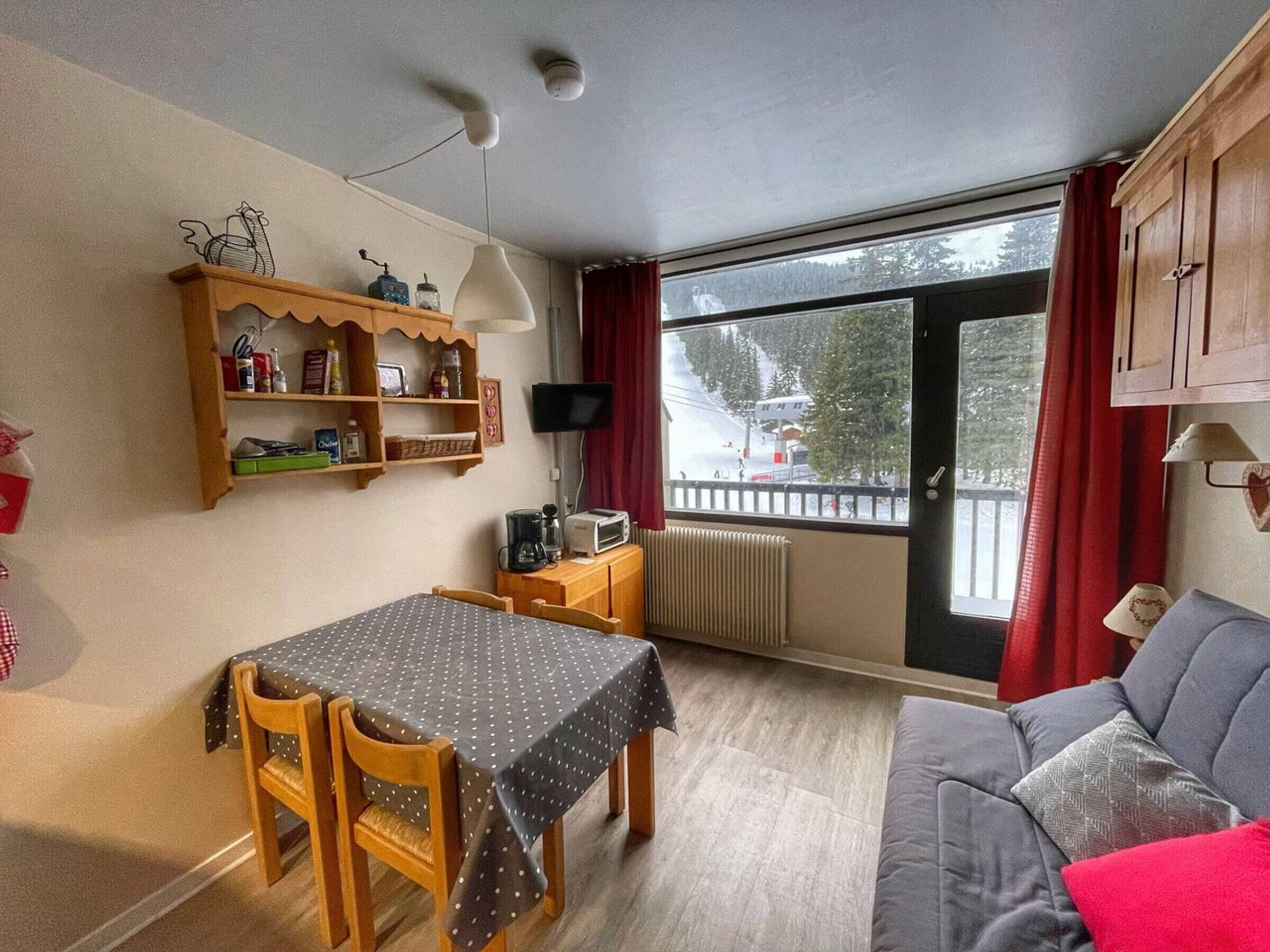 A cozy room with a dining table, chairs, a sofa, a TV, and a window with a view of a snowy landscape.