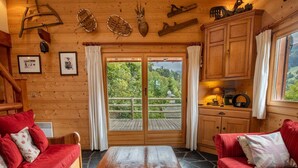 Un acogedor interior de cabaña con una mesa de comedor de madera, sofás tapizados en rojo y un ventanal con vistas al bosque circundante.