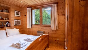 Una habitación tipo cabaña de madera con una cama, una ventana con cortinas y una estantería con libros y maquetas de casas.