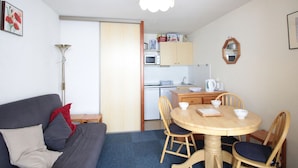 A compact living space with a sofa, a dining table with chairs, a kitchenette, and a ceiling light. - Cozy Studio for 5 in Sagittaire Residence, Near Slopes, South-Facing Balcony (Flaine)