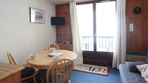 A room with a wooden dining table, chairs, a television mounted on the wall, a balcony with a view, and a bed with a blue carpet. - Cozy Studio for 5 in Sagittaire Residence, Near Slopes, South-Facing Balcony (Flaine)