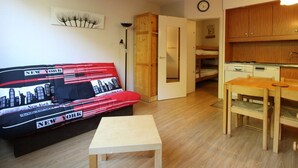 A compact living space with a sofa, a small table, a kitchenette, and a door leading to another room.