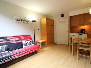 A compact room with a bed, a small table, a chair, a kitchenette, and a wardrobe.