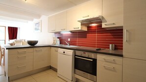 Een moderne keuken met lichte kastjes, een rode tegelachtergrond, een vaatwasser en een inbouwoven.