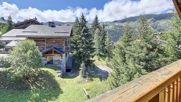 Una baita di legno con fondamenta in pietra, circondata da un fitto bosco e montagne sullo sfondo.