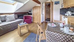 Un accogliente loft con letto a soppalco, un tavolo da pranzo per due persone, un angolo cottura e un’area salotto con divano e poggiapiedi decorato.