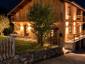 A wooden cabin with a stone wall and a tree in front.