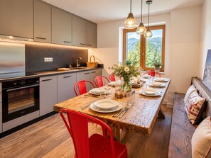 A modern kitchen with built-in appliances, a dining area with a wooden table set for four, and a view of mountains through a window.