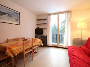 A room with a dining table, chairs, a TV, a balcony with curtains, and a red bed. - Renovated Studio for 5 in Flaine Forest, Close to Slopes and Shops (Flaine)