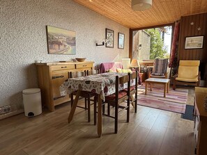 Ein gemütliches Zimmer mit Holzbalkendecke, einem Esstisch mit Stühlen, einem Bett mit einem gemusterten Überwurf und einem Fenster mit Blick auf Grünflächen.