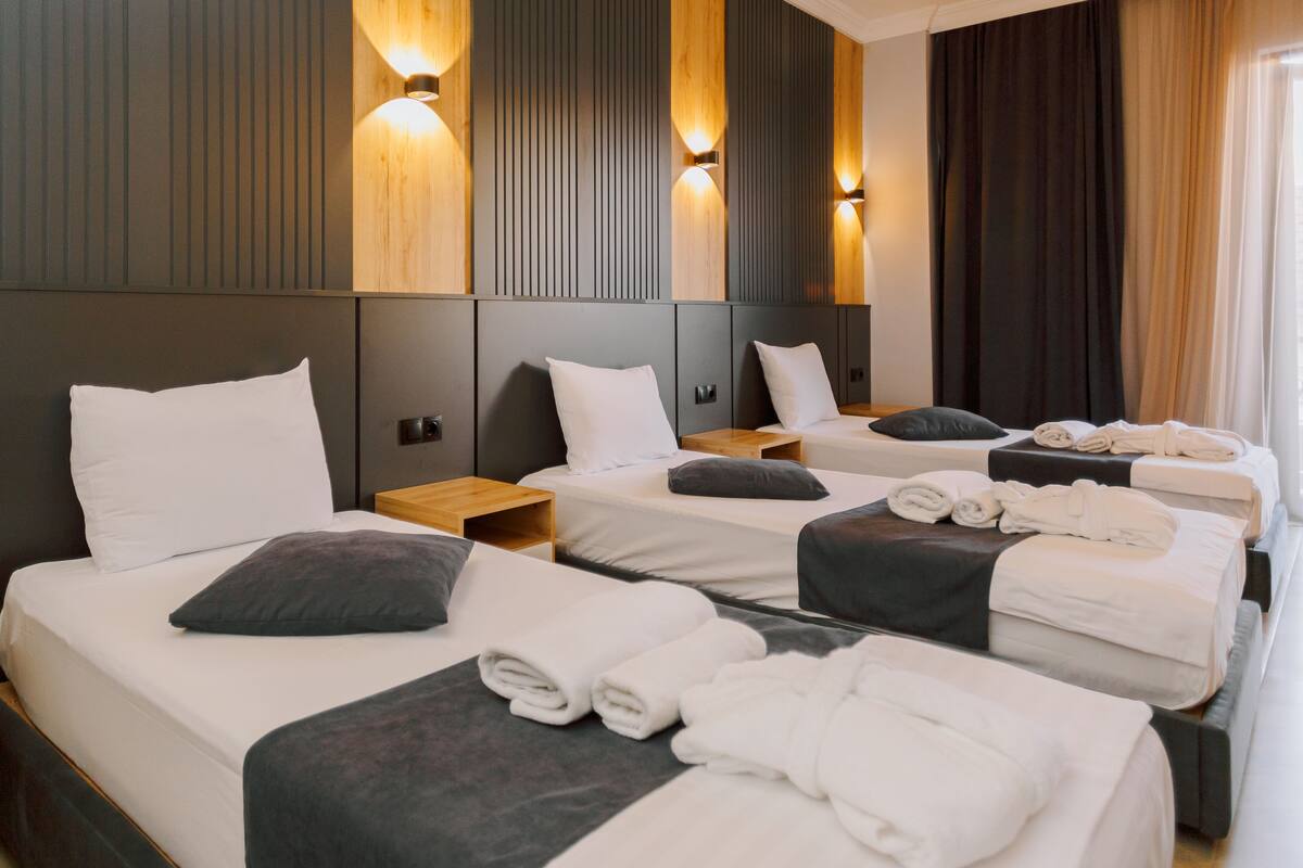 A hotel room with three beds, each with white linens and towels, wooden headboards, and wall-mounted light fixtures.